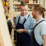 Portrait of senior carpenter talking to young trainee while working in joinery workshop, copy space
