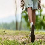 Low angle shot of a Black woman hiker's legs and feet as she walks along a grassy trail in a lush forest, enjoying an outdoor adventure.