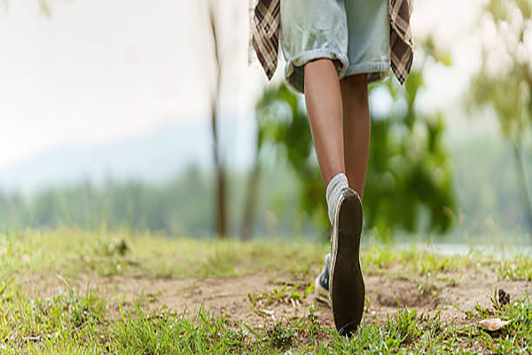 Low angle shot of a Black woman hiker's legs and feet as she walks along a grassy trail in a lush forest, enjoying an outdoor adventure.