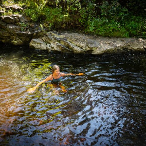 A mature woman enjoying the restorative power of nature.  She is wild swimming in a beautiful stream